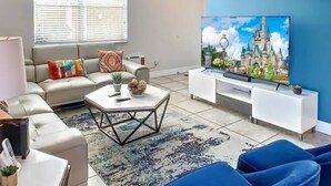 A living room with a large flat-screen TV, a sofa, a coffee table, and a blue chair. - Mandalorian Retreat – Private Pool Near Disney (Kissimmee)