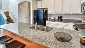 A modern kitchen with granite countertops, stainless steel appliances, and white cabinetry. - Mandalorian Retreat – Private Pool Near Disney (Kissimmee)