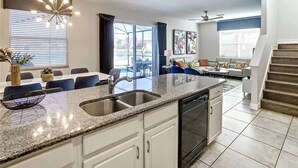 A modern kitchen with a granite countertop, built-in dishwasher, and a dining area with a table and chairs. - Mandalorian Retreat – Private Pool Near Disney (Kissimmee)