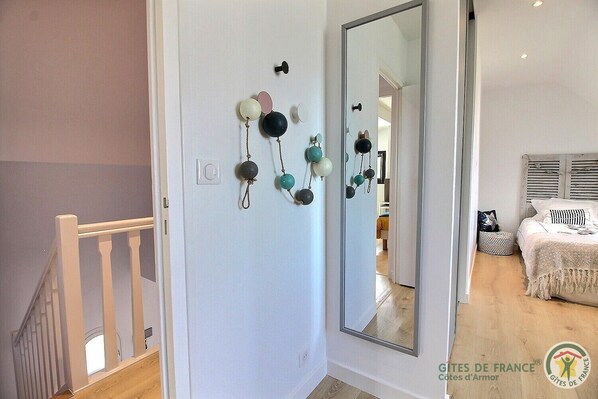 A bedroom with a large mirror, a bed with a white cover, and a small bedside table.