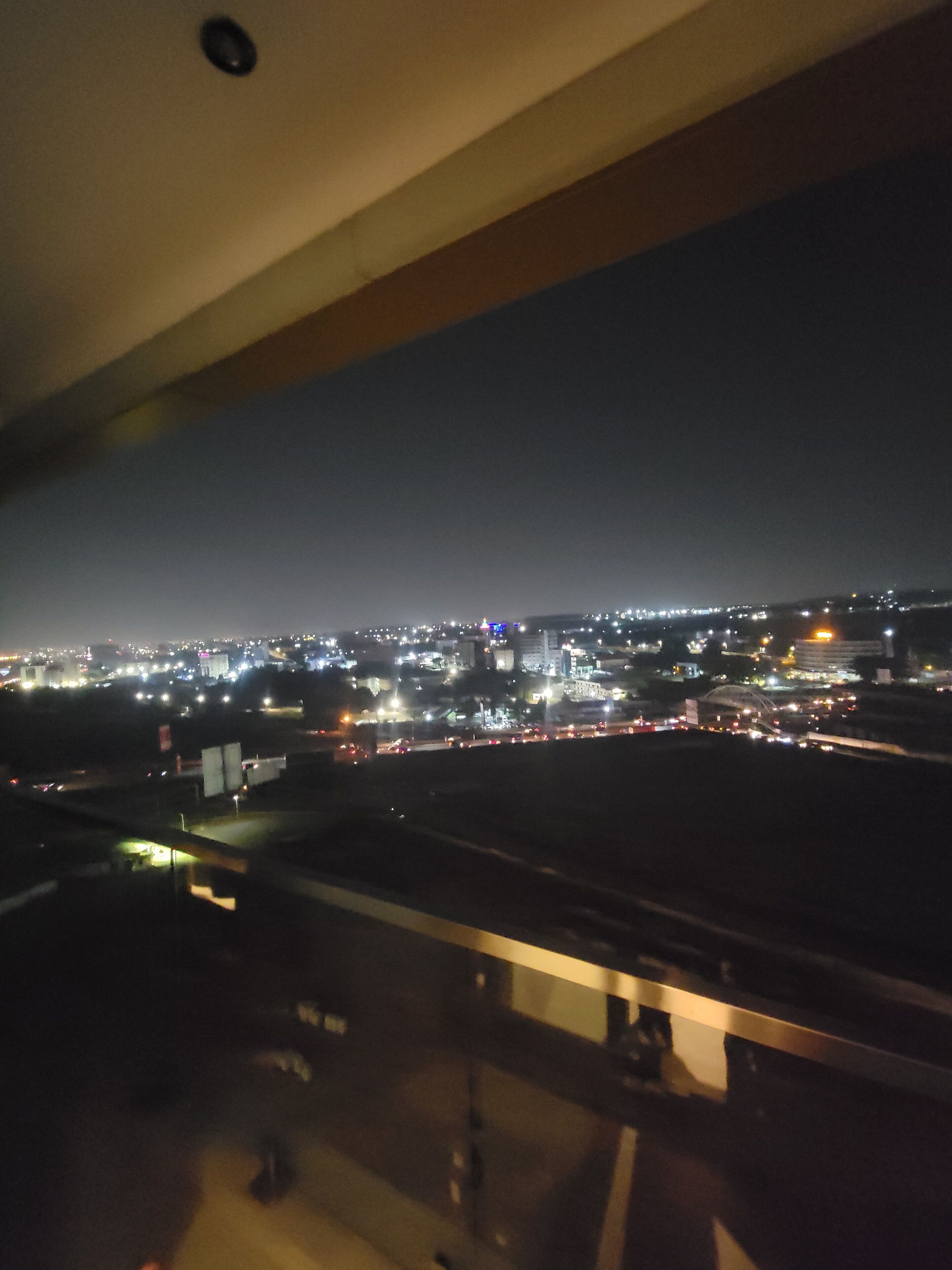 A nighttime cityscape viewed from a balcony with a railing.