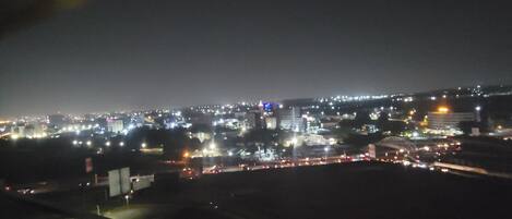 A nighttime cityscape viewed from a balcony with a railing.