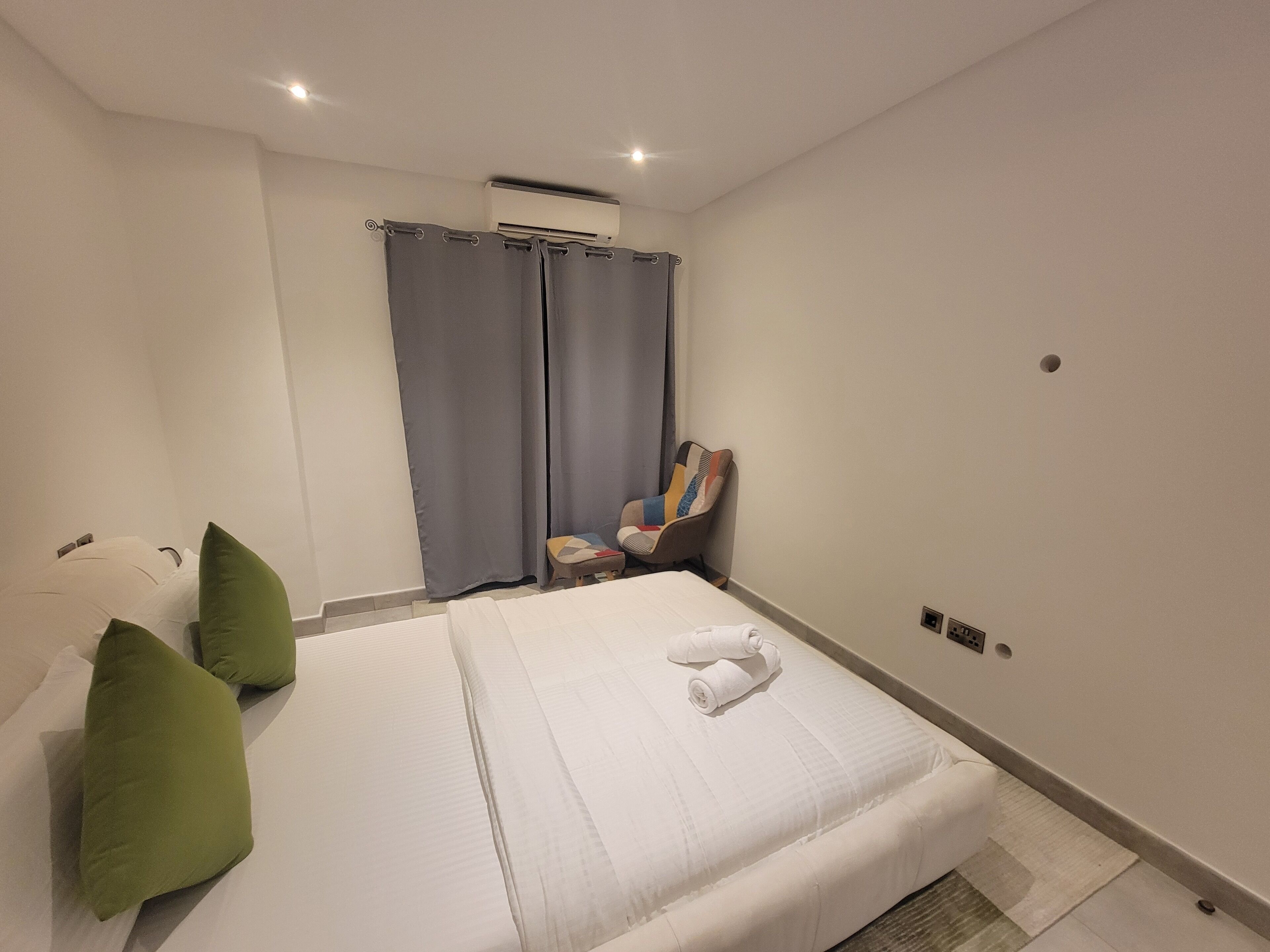 A hotel room with a bed, pillows, a chair, and a curtain.