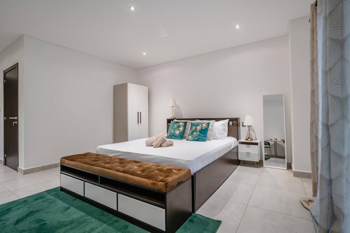 A modern bedroom with a bed, a bench, a wardrobe, and a nightstand.