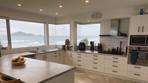 A modern kitchen with a large island, white cabinetry, and a view of the ocean. - Ultimate Beachfront - Family Friendly with games room and multiple decks (Waimarama)