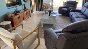 A living room with a large TV, wooden furniture, a coffee table, and a view of the beach. - Ultimate Beachfront - Family Friendly with games room and multiple decks (Waimarama)