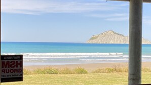 A view of a beach with waves and a distant mountain. - Ultimate Beachfront - Family Friendly with games room and multiple decks (Waimarama)