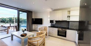 A modern kitchen with a flat-screen TV, a dining area with wicker chairs, and a view of the outdoors.