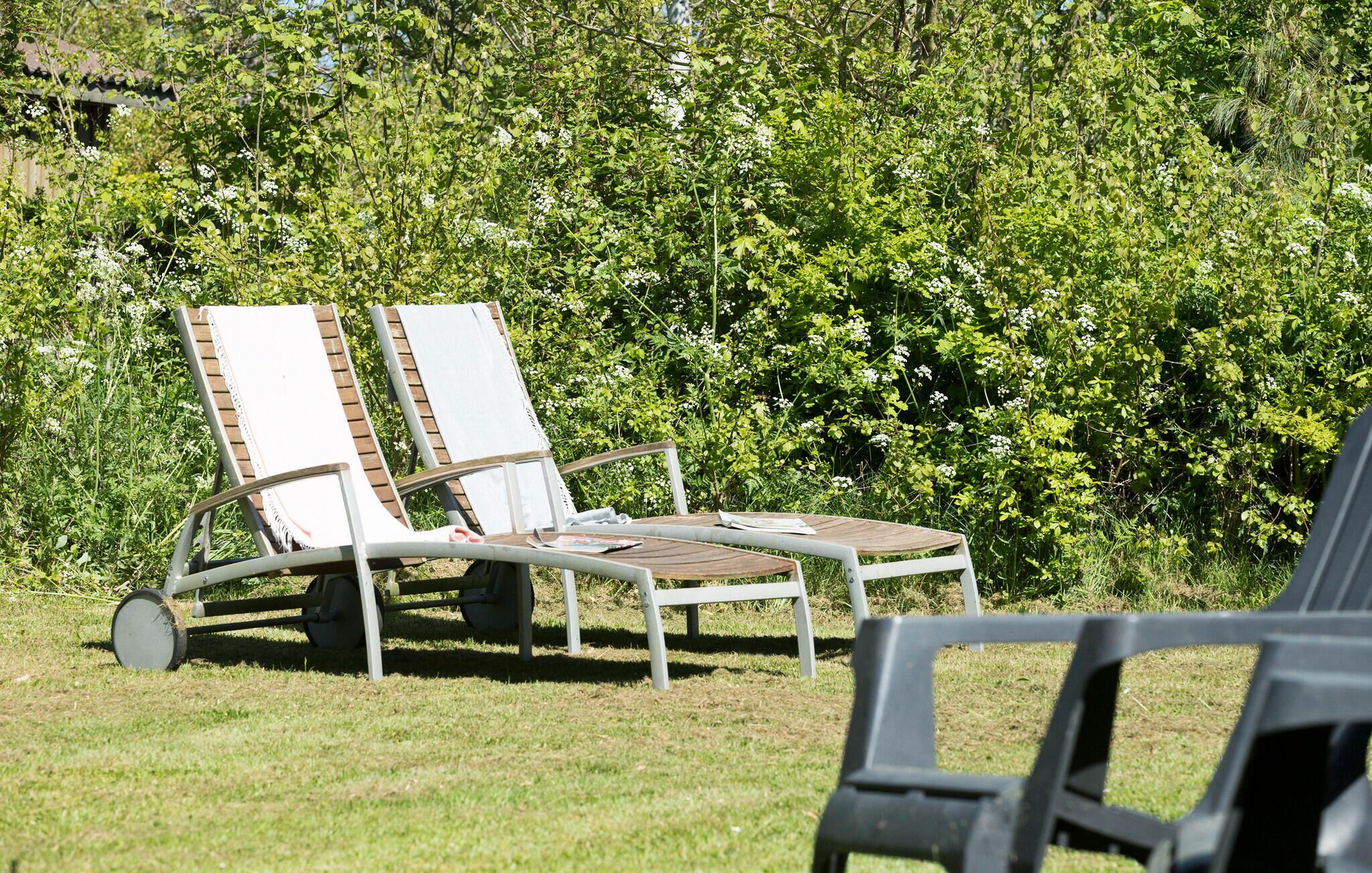 Deux chaises longues dotées d’une structure en métal et d’assises en lattes de bois, placées sur une pelouse verdoyante, avec un feuillage dense en arrière-plan.