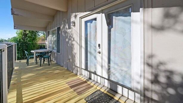 A covered outdoor area with a wooden deck, a table with chairs, and a sliding glass door. - Home located close to Downtown (Spearfish)