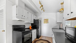 A compact kitchen with white cabinets, a black stove, a black refrigerator, and a microwave. - Home located close to Downtown (Spearfish)