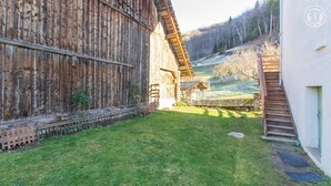 Un granero rústico con fachada de madera, un patio cubierto de césped y un edificio blanco con una escalera.