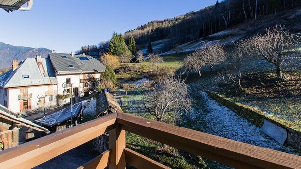 Terraza de madera con vistas a un paisaje rural que incluye casas y un río.