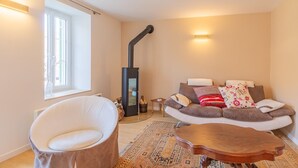 Una sala de estar acogedora con un sofá, una silla blanca, una mesa de centro de madera, una chimenea y una ventana.
