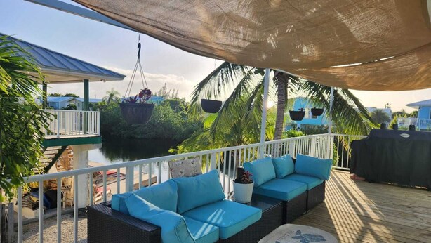 A covered outdoor seating area with a sofa and a round table, overlooking a body of water and greenery. - Christmas in the FL Keys!!! Stunning sunsets, beaches 10 min away, Fishing!!! (Big Pine Key)
