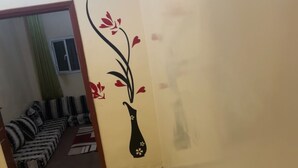 A narrow hallway with patterned floor tiles, a sofa with striped cushions, and a wall decoration of a vase with flowers. - Résidence Mouna (Nouadhibou)