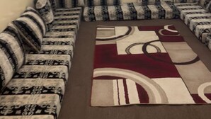 A living room with a sofa set, a patterned rug, and two windows with bars. - Résidence Mouna (Nouadhibou)