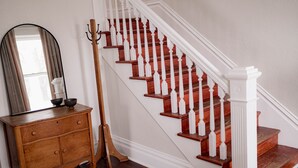 A staircase with wooden steps and white balusters, a wooden dresser with a mirror, and a coat rack.