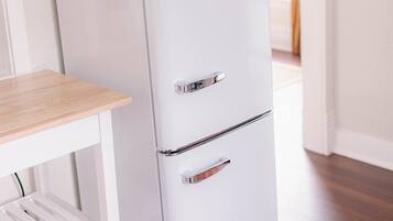 A white Classic refrigerator in a room with wooden flooring and a white table with shelves.