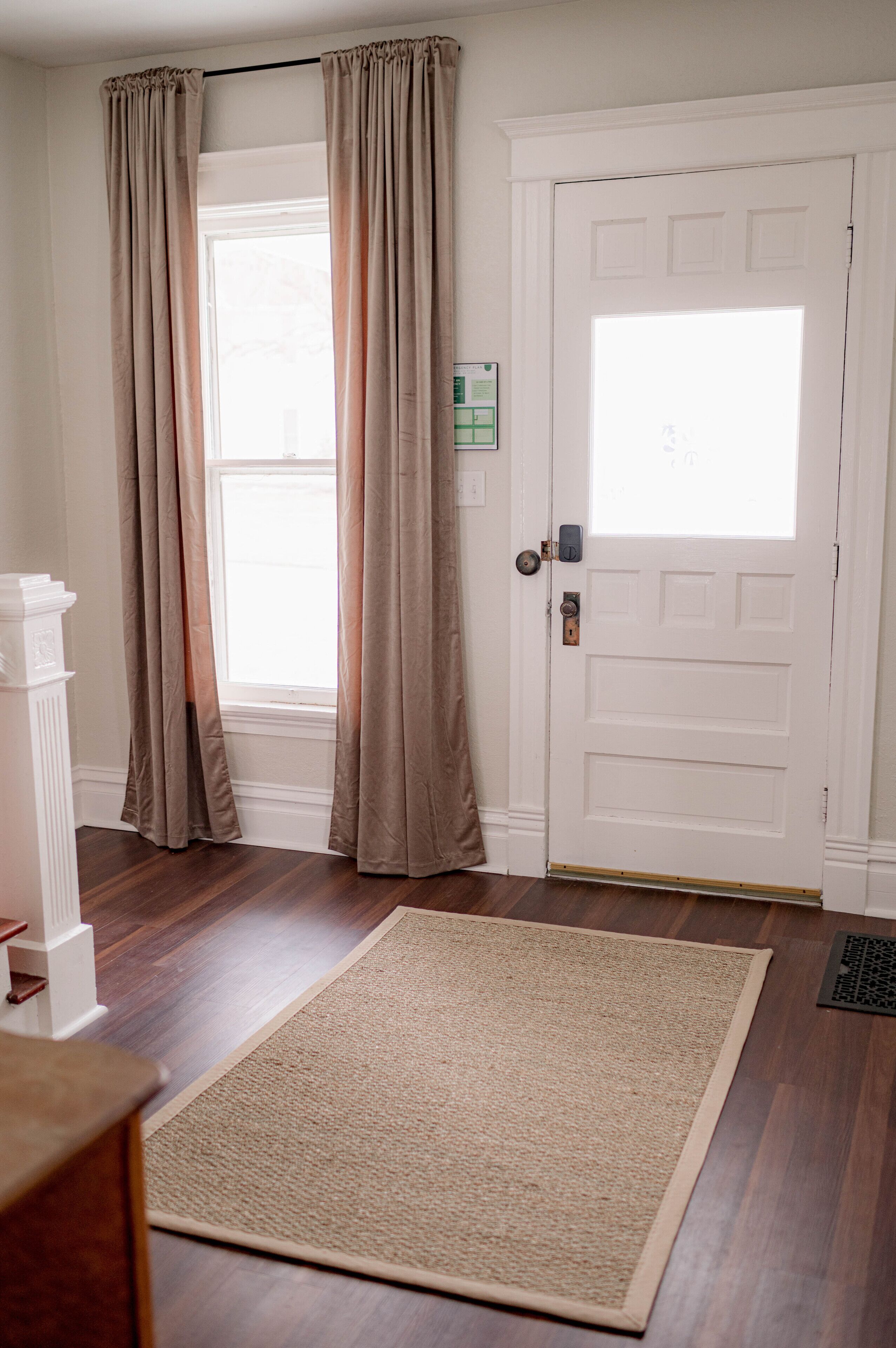 A room with a white door, beige curtains, a beige rug, and a white column.
