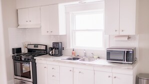 A modern kitchen with white cabinets, a stainless steel stove, a coffee maker, a microwave, and a sink.
