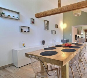 A modern kitchen with a wooden dining table, clear chairs, and built-in shelves with plants.