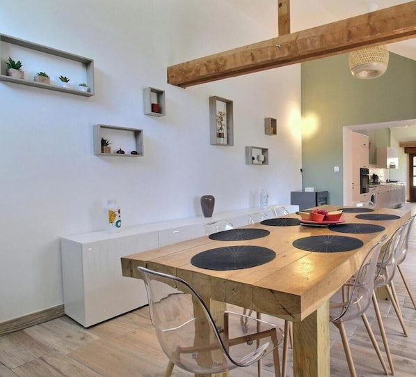 A modern kitchen with a wooden dining table, clear chairs, and built-in shelves with plants.