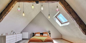 A bedroom with a sloped ceiling, a skylight, a bed with orange bedding, a white dresser, and a radiator.