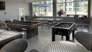 Un espace de loisirs intérieur moderne, doté de tables de billard, d’un baby-foot et de sièges confortables.