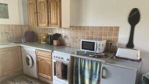 A compact kitchen with wooden cabinets, a washing machine, a microwave, and a toaster. - Sunrise - A beautiful 2 bedroom Gite in the unspoiled countryside of the Cruese (CHENIERS)