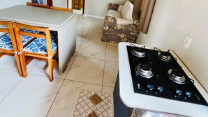 Cocina compacta con estufa a gas, sillas de madera, una pequeña mesa de comedor y un tapete estampado.