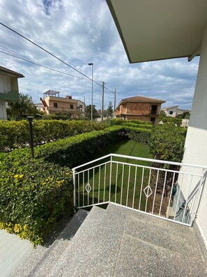 Zona residencial con un camino pavimentado, barandilla de metal blanco y un seto bien cuidado.