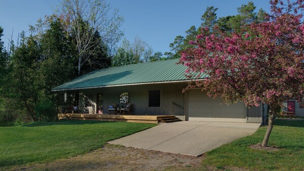 A single-story house with a green metal roof, a front porch with a bench, and a garage. - River Cottage Retreat - Close to Golf, Beaches, Hiking! (Thompsonville)