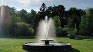 Una fuente circular con chorros de agua en un parque arbolado.