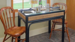 Un comedor con una mesa dispuesta para dos, una ventana que ofrece vistas a un paisaje verde y una puerta de madera.