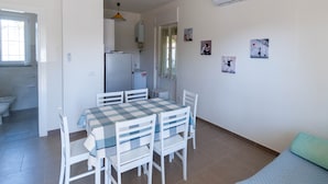 Un comedor con una mesa de cuadros y sillas blancas, una cocina al fondo y una pared con cuadros enmarcados.