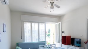 Una habitación con una mesa de comedor, sillas, un sofá, un ventilador de techo, un televisor y una ventana con cortinas.