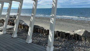 A wooden deck with a white pergola overlooking a pebble beach and ocean. - Modern Mid-Century Cabin, on the beach, with views of the San Juan Islands! (Oak Harbor)
