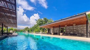 A clear blue pool with lounge chairs and umbrellas, surrounded by greenery and modern architecture.