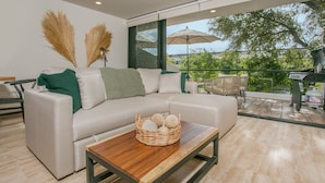 A modern living room with a sofa, a wooden coffee table, and a view of the outdoors.