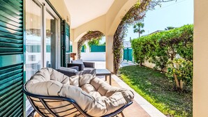 An outdoor seating area with a cushioned chair and table, a covered patio, and a view of a well-maintained garden. - Monteiro V4 - VIP Properties by Interhome (Albufeira)