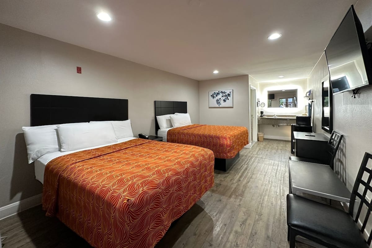 A hotel room with two beds, a desk, a chair, a TV, and a bathroom visible in the background.