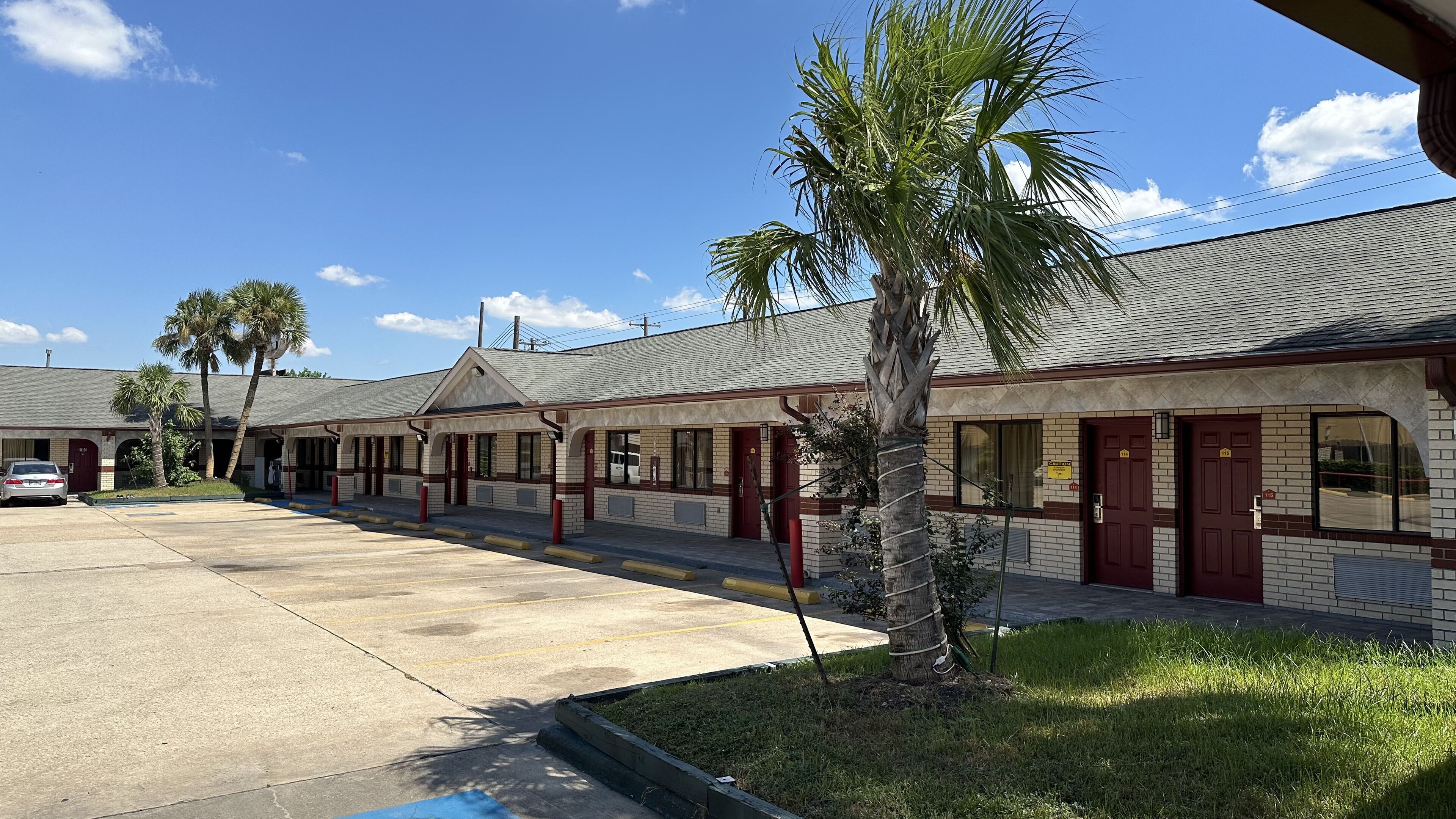 A motel with multiple rooms, a parking lot, and palm trees.