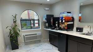 A modern kitchen with a marble floor, a large window, a plant, a fruit juice dispenser, and a coffee machine. - Palace Inn I-45 & Bellfort (Houston)
