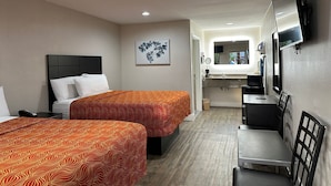 A hotel room with two beds, a desk, a chair, a TV, and a bathroom visible through an open door. - Palace Inn I-45 & Bellfort (Houston)