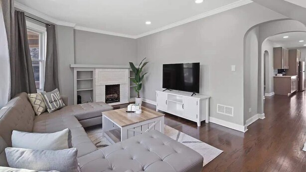 A modern living room with a sectional sofa, a flat-screen TV, a fireplace, and a kitchen in the background. - Bungalow w/ Game Room | LCP Collection (Morton Grove)