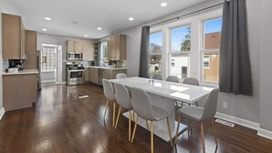 A modern kitchen with a dining area, wooden flooring, and large windows. - Bungalow w/ Game Room | LCP Collection (Morton Grove)