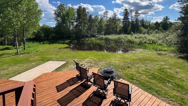 Une terrasse en bois avec des meubles d’extérieur, un foyer et un étang, le tout situé dans un espace boisé.