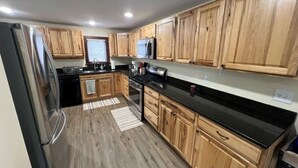 Une cuisine avec des meubles de rangement en bois, un plan de travail noir, un réfrigérateur, une cuisinière et un four à micro-ondes.