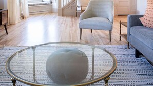 A spacious living room with a staircase, a glass coffee table, and a blue ottoman. - Hale House, Customizable Historic Gem in downtown Bayfield (Bayfield)
